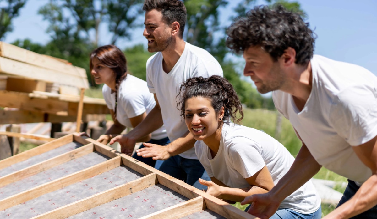 Volunteers in white t-shirts lift wood frame.